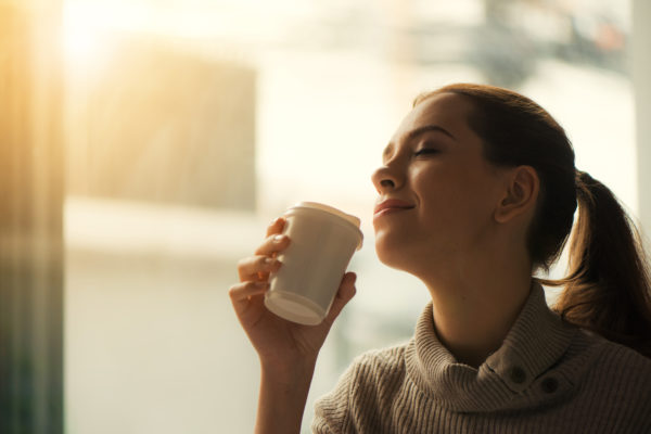 Woman drinking coffee at home with sunrise streaming in through